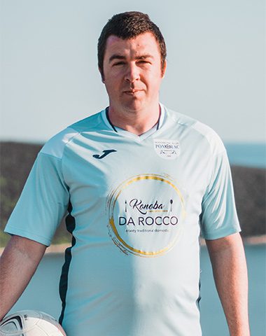 A man in a light blue shirt is standing by the water.