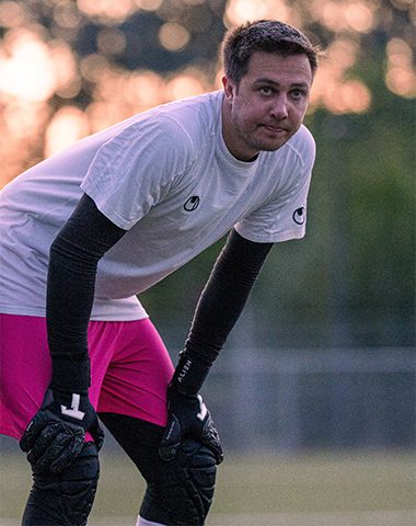 A man in pink shorts and white shirt holding gloves.