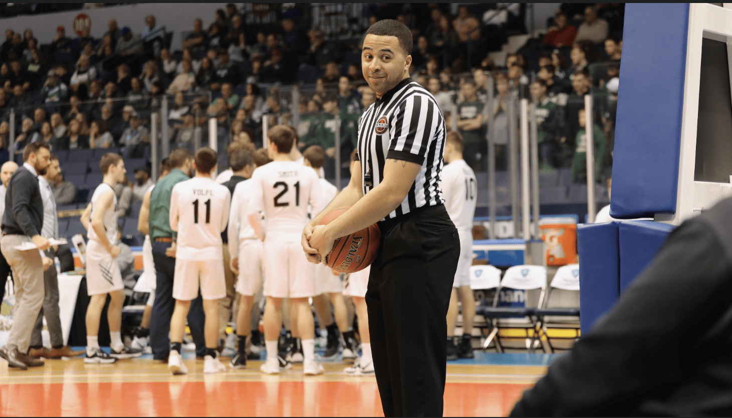 A referee holding a basketball in front of the crowd.