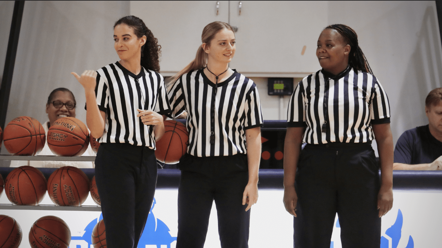 Three women in referee uniforms holding a basketball.